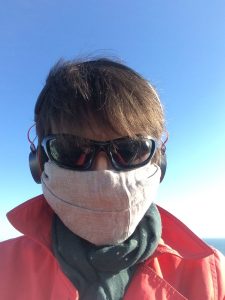 Naomi outside in her mask, with sunglasses and headphones.