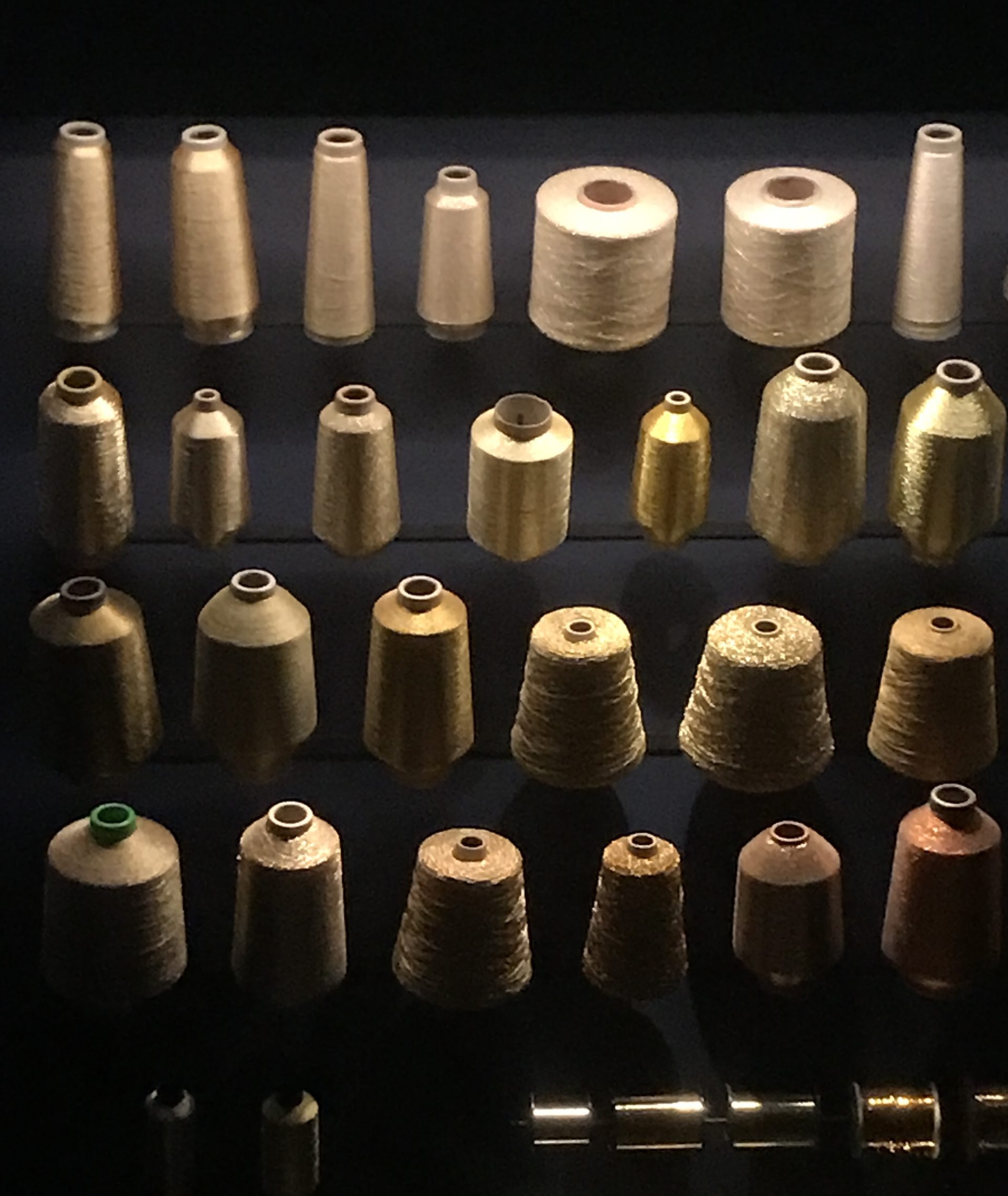 A museum case full of bobbins of gold thread.